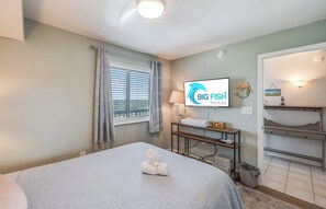 A hotel room with a bed, a TV displaying 'BIG FISH Rentals', a window with curtains, a bedside table with a lamp, and a view of the outside. - 3BR at Ocean Bay Club, Pools with Oceanview Condo (North Myrtle Beach)