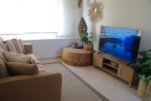 A living room with a sofa, a TV, a wooden side table, and a window. - Oasis in El Chante Pool Near the Malecón (Chantepec)