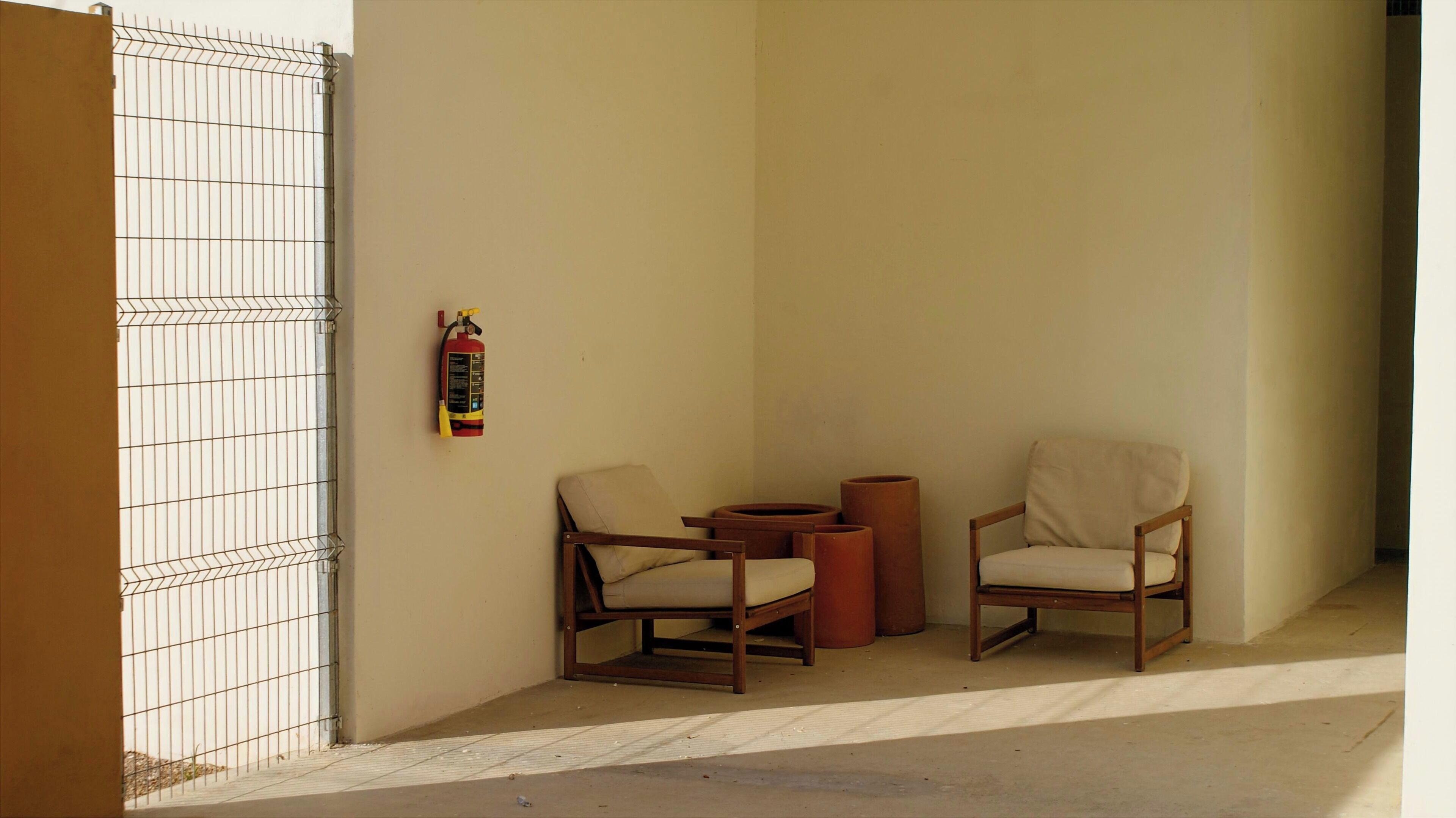 A corner of a room with two chairs, a small table, and a fire extinguisher on the wall.
