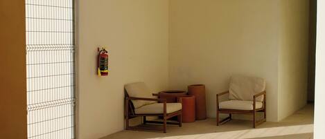 Un coin de pièce avec deux chaises, une petite table et un extincteur accroché au mur.