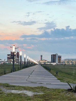 A pathway leading to a building complex with multiple floors and a tall tower, surrounded by greenery and street lamps.