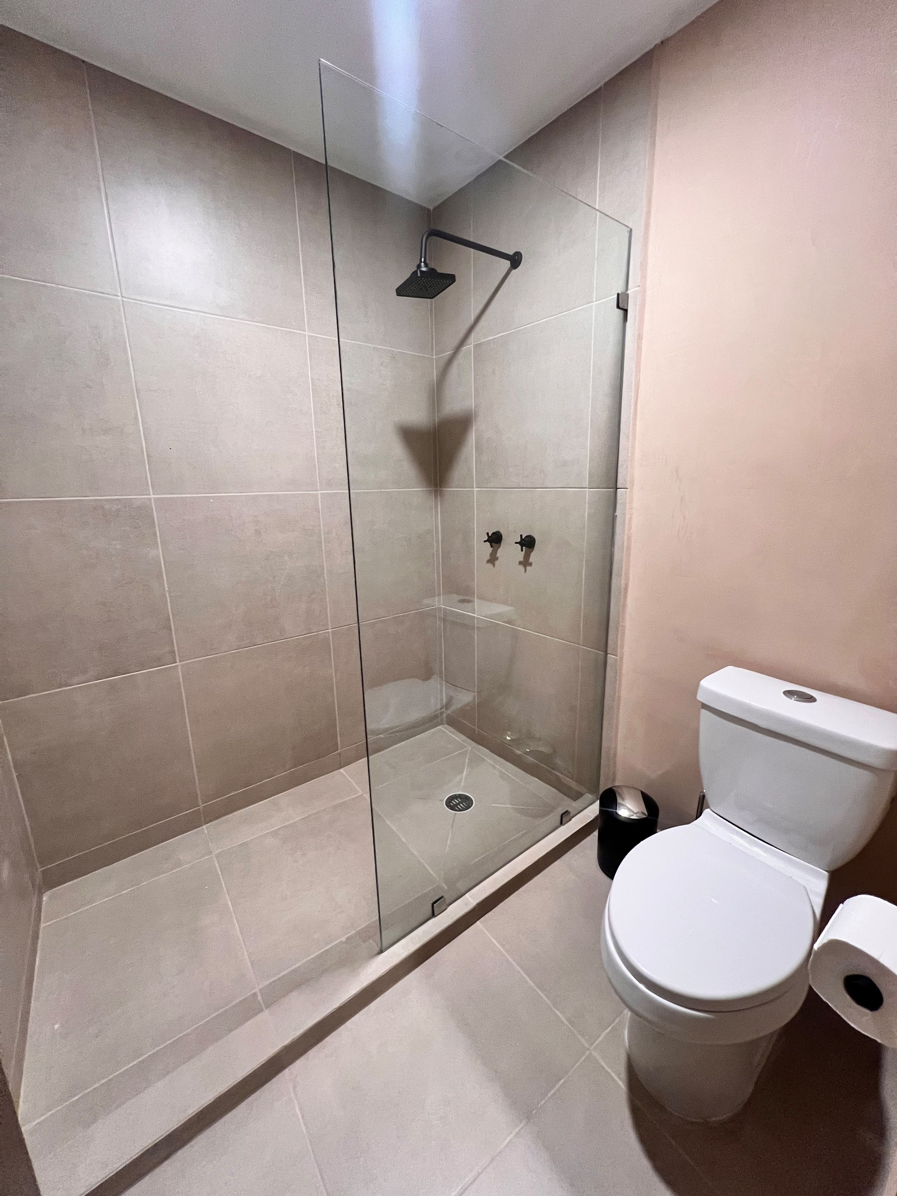 A bathroom with a glass-enclosed shower, a toilet, and a trash bin.