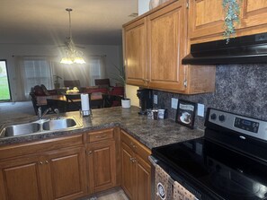 A kitchen with wooden cabinets, a stainless steel sink, a black stove, and a coffee maker. - Fort Benning & Columbus, Ga - Home Away From Home (Columbus)