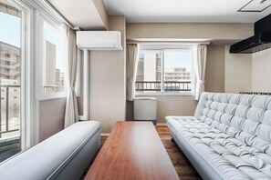 A modern living room with a sofa, a wooden table, and a window with curtains. - TetiTeti (Sapporo)