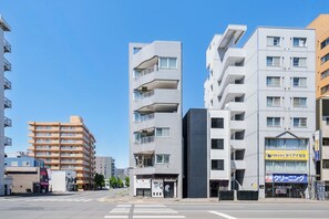 A multi-story building with balconies, a crosswalk, and a clear sky. - TetiTeti (Sapporo)