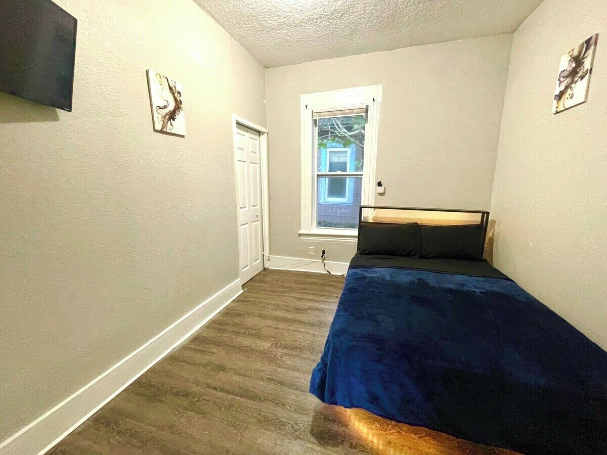 Une chambre à coucher avec un lit, une porte, une fenêtre et une œuvre d’art accrochée au mur.