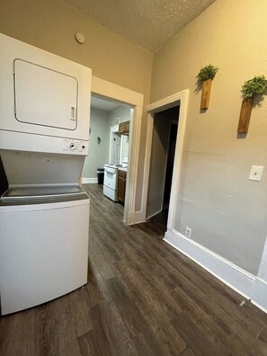 A laundry room with a washer and dryer, a wooden floor, and a doorway leading to a kitchen area. - Comfy 3/1 With Everything You Need - 5 Mins to DT (Jacksonville)