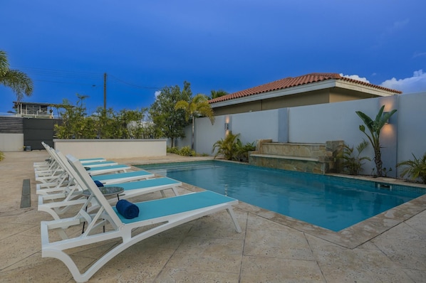 A swimming pool with lounge chairs and a stone-tiled deck.