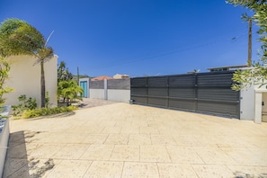 A paved driveway leading to a gated entrance with a modern building and a clear blue sky.