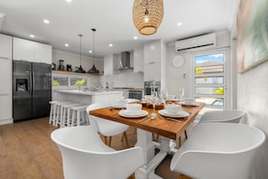 A modern kitchen with white cabinetry, a stainless steel refrigerator, and a dining area with white chairs and a wooden table. - Private 3BR2BA Villa w/ Private Pool & Close2Beach (Noord)