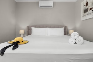 A hotel room with a bed, two bedside lamps, an air conditioner, and rolled towels. - Private 3BR2BA Villa w/ Private Pool & Close2Beach (Noord)