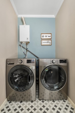 A laundry room with two front-loading LG washers, a white utility box, and a framed sign with laundry instructions.