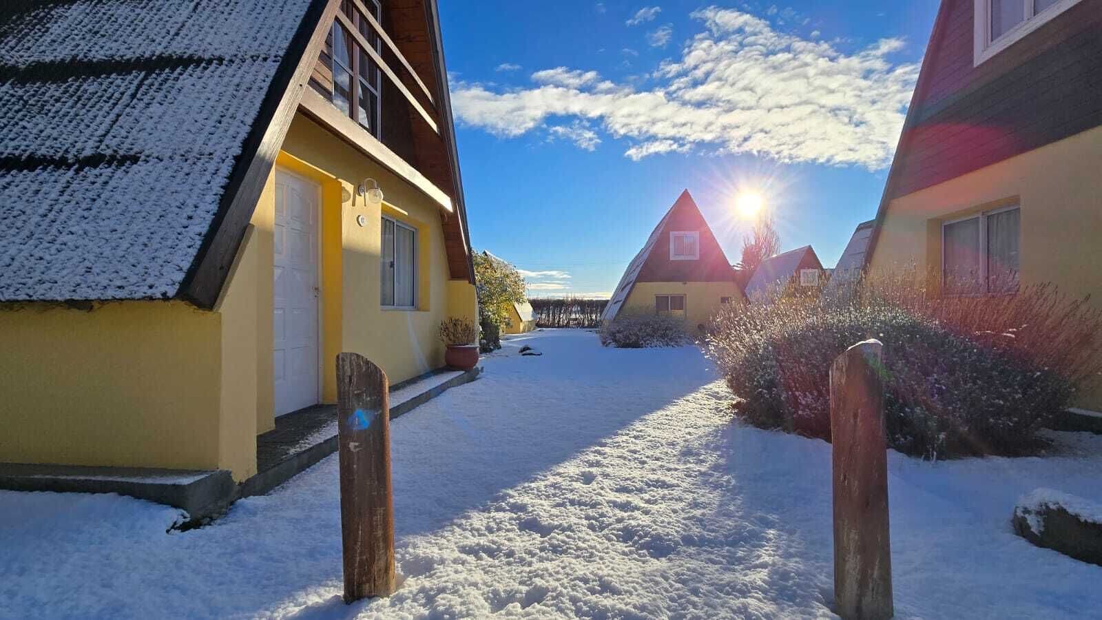 Un sentier enneigé mène à une rangée de maisons, sous un ciel dégagé et baigné de soleil.