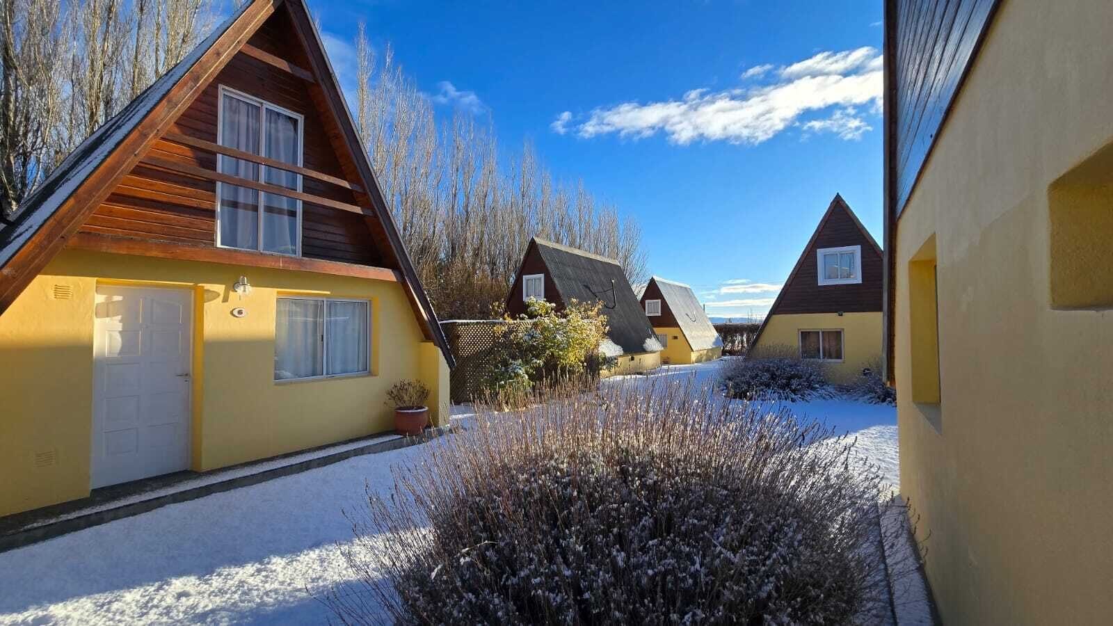 Una hilera de casas de madera con techos inclinados, suelo cubierto de nieve y cielo despejado.