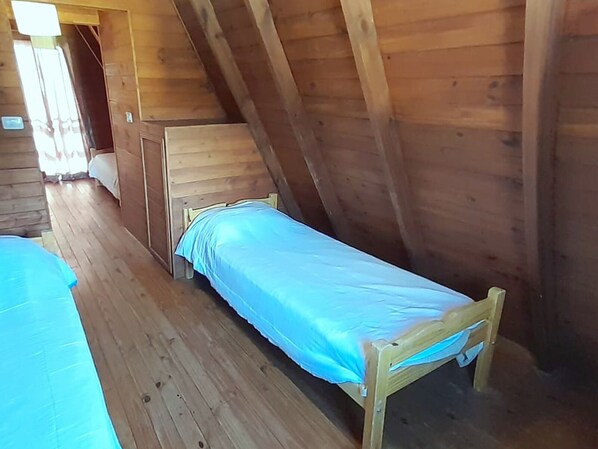 A single wooden bed in a cabin with a sloped ceiling.