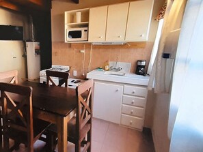 A compact kitchen with a microwave, stove, and sink. There is a dining table with chairs.