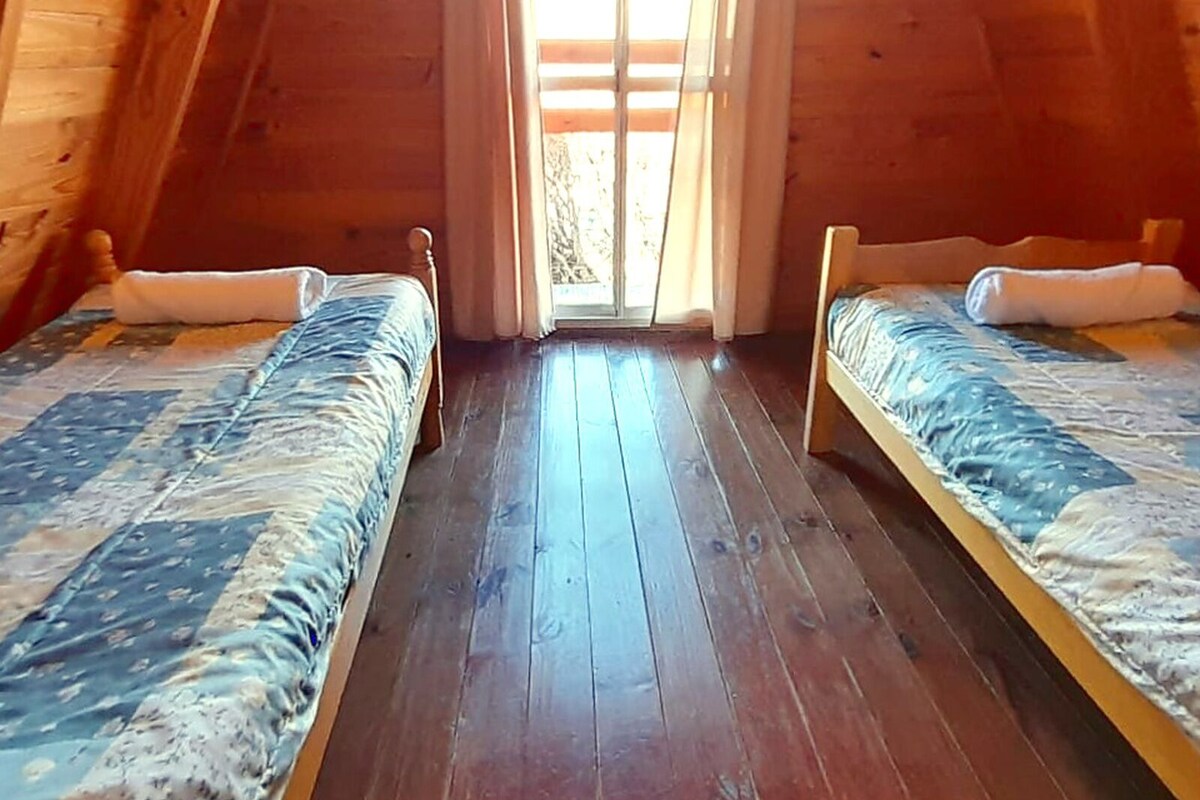 A small, cozy attic bedroom with two beds, wooden floors, and a large window.