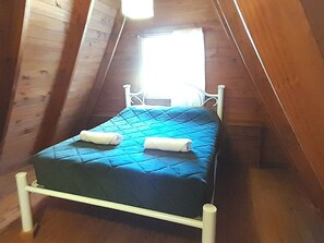 A single bed with a blue quilt and two rolled towels, in a room with wooden walls and a sloped ceiling.