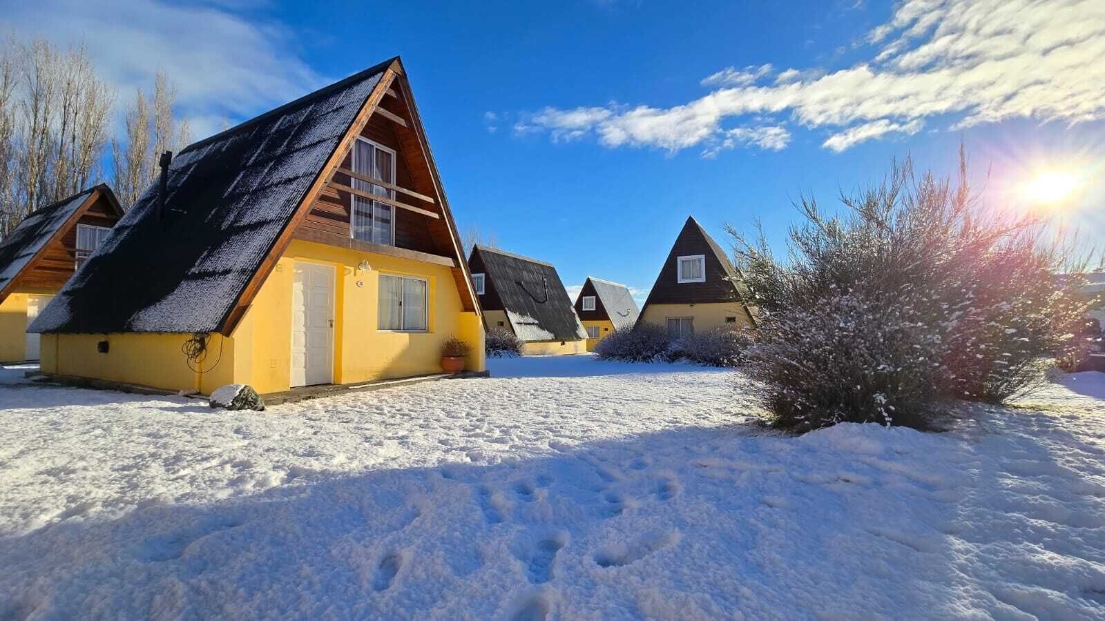 Een rij hutten met schuine daken, omgeven door sneeuw, onder een heldere lucht.