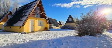 Une rangée de cabanes aux toits inclinés, entourées de neige, sous un ciel dégagé.
