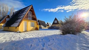 A row of cabins with sloped roofs, surrounded by snow, under a clear sky.