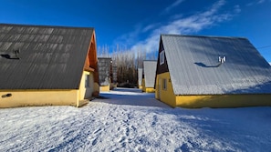 A row of cabins with sloped roofs, a clear sky, and a snow-covered ground.