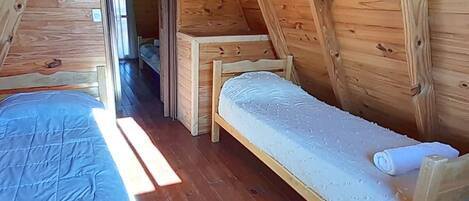 A small, wooden, attic-style room with two bunk beds and a narrow hallway.