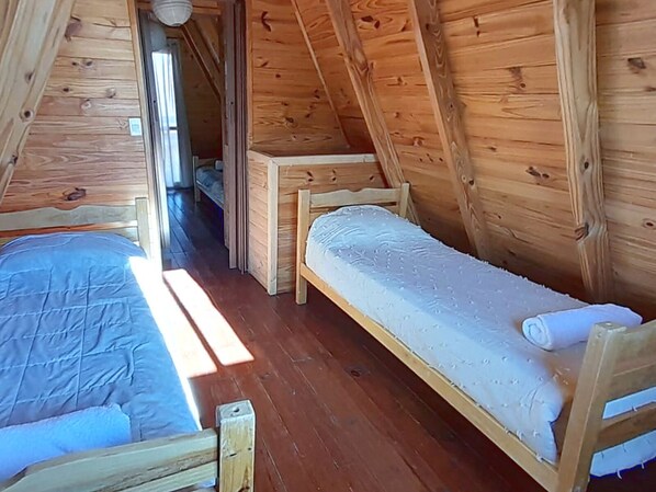 A small, wooden, attic-style room with two bunk beds and a narrow hallway.
