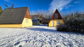 Schneebedeckte Landschaft mit zwei Gebäuden, eines gelb und eines braun, unter wolkenlosem Himmel.