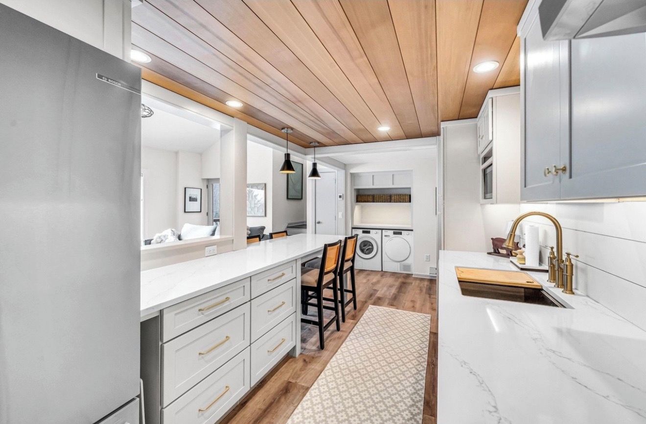 A modern kitchen with white cabinetry, a wooden ceiling, and a marble countertop.