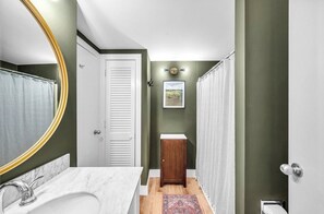 Ein Badezimmer mit einem weißen Waschbecken, einem Spiegel mit goldener Rahmung, einem Holzschrank und einer Duschvorhang.