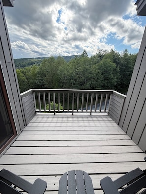 A wooden deck with a railing, two chairs, and a view of a forested area. - Summit View Retreat (Dover)