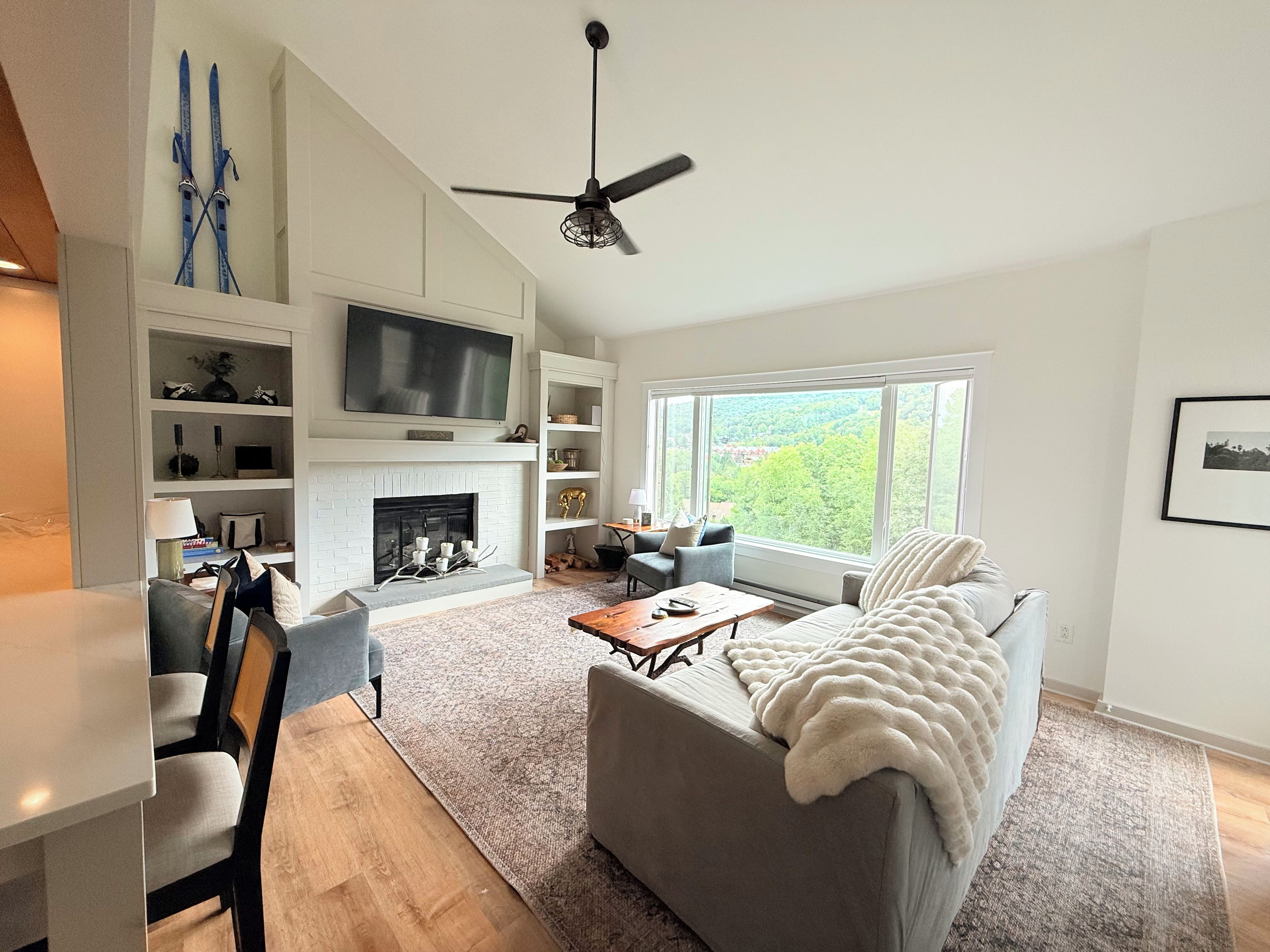 A modern living room with a fireplace, a television, and a large window offering a view of the outdoors.