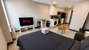 Quarto de hotel moderno com uma cama grande, televisão, cozinha compacta e área de estar.