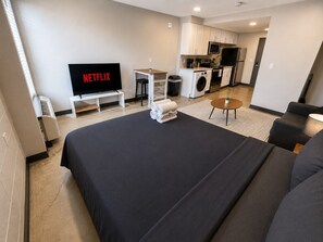Ett modernt hotellrum med en stor säng, en TV, en liten köksdel och en sittgrupp.