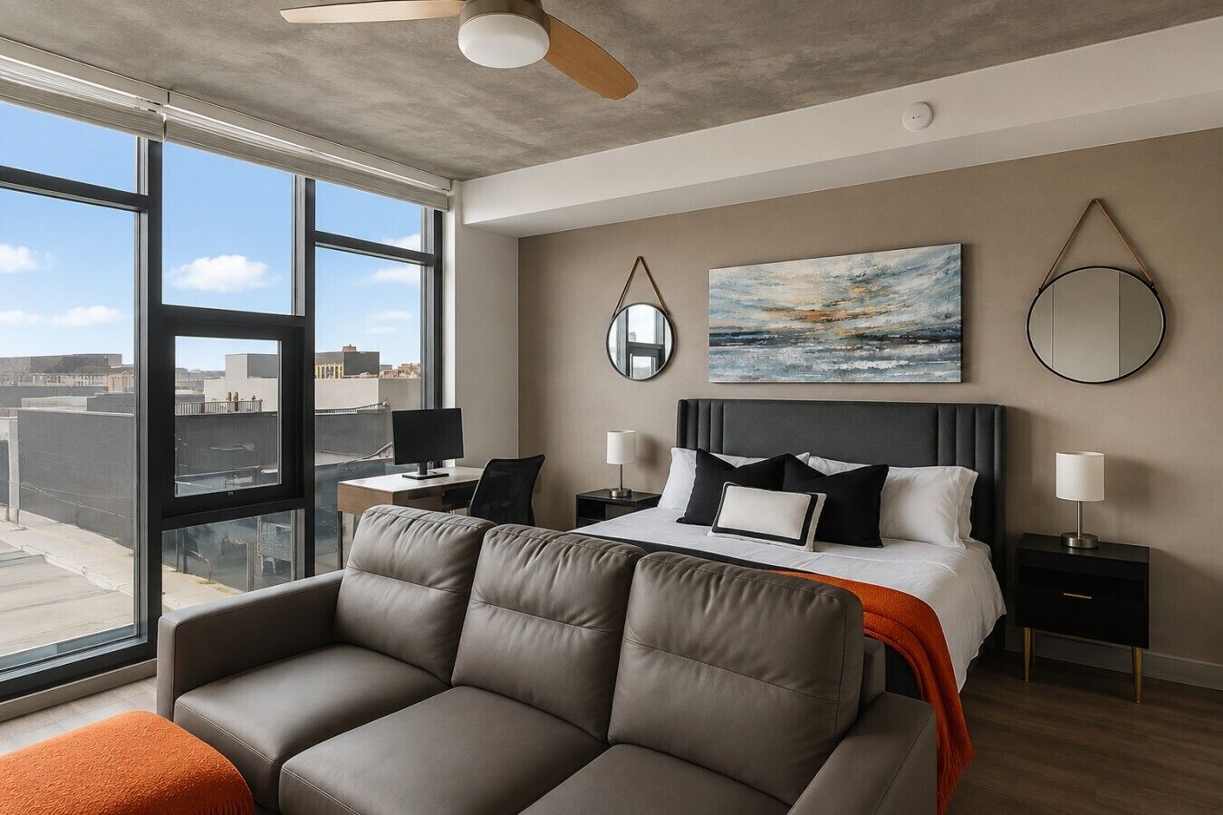 A modern hotel room with a large bed, a sofa, a desk, and a view of the city.