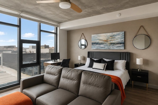 A modern hotel room with a large bed, a sofa, a desk, and a view of the city. - Stylish Studio | Skyline Views + Pool (Birmingham)