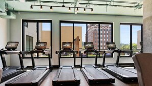 Ein Fitnessstudio mit in Reihen angeordneten Laufbändern, großen Fenstern und Blick auf Gebäude im Freien.