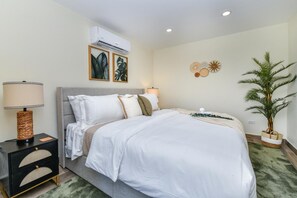 Une chambre d’hôtel comprenant un lit, une lampe de chevet, un appareil de climatisation, des éléments de décoration murale et une plante en pot.