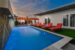 Une piscine dotée de chaises longues, d’une cascade et d’un espace patio avec des sièges d’extérieur.