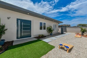 Une maison moderne avec une porte bleue, un petit jardin avec du gazon synthétique et un banc en bois.