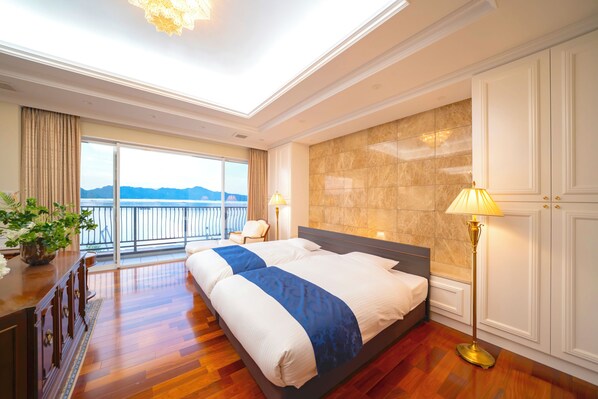 A hotel room with a large bed, a desk, a chair, a lamp, and a view of the sea.