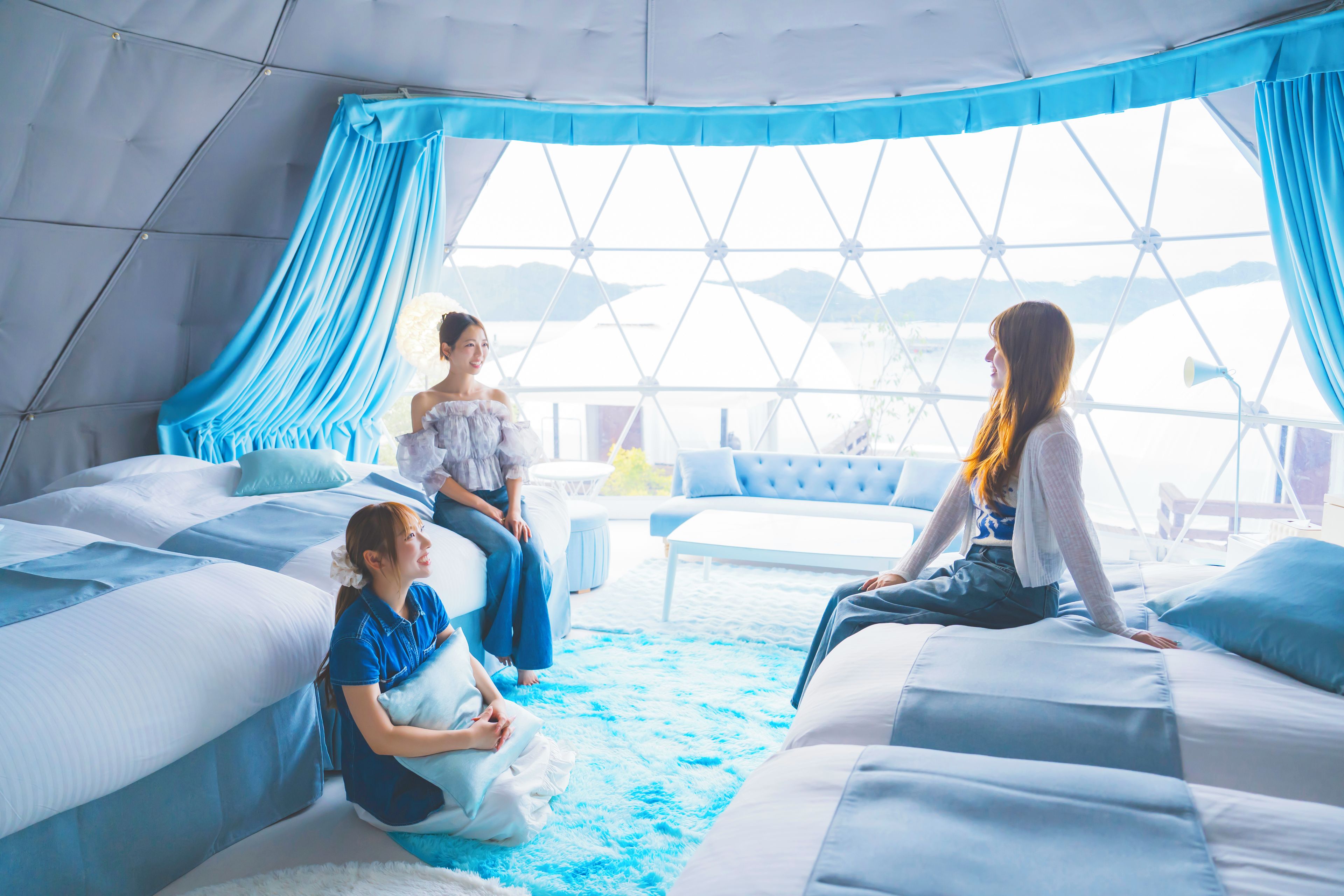 Una habitación con techo geométrico, un ventanal con cortinas y una cama con un tapete azul mullido.
