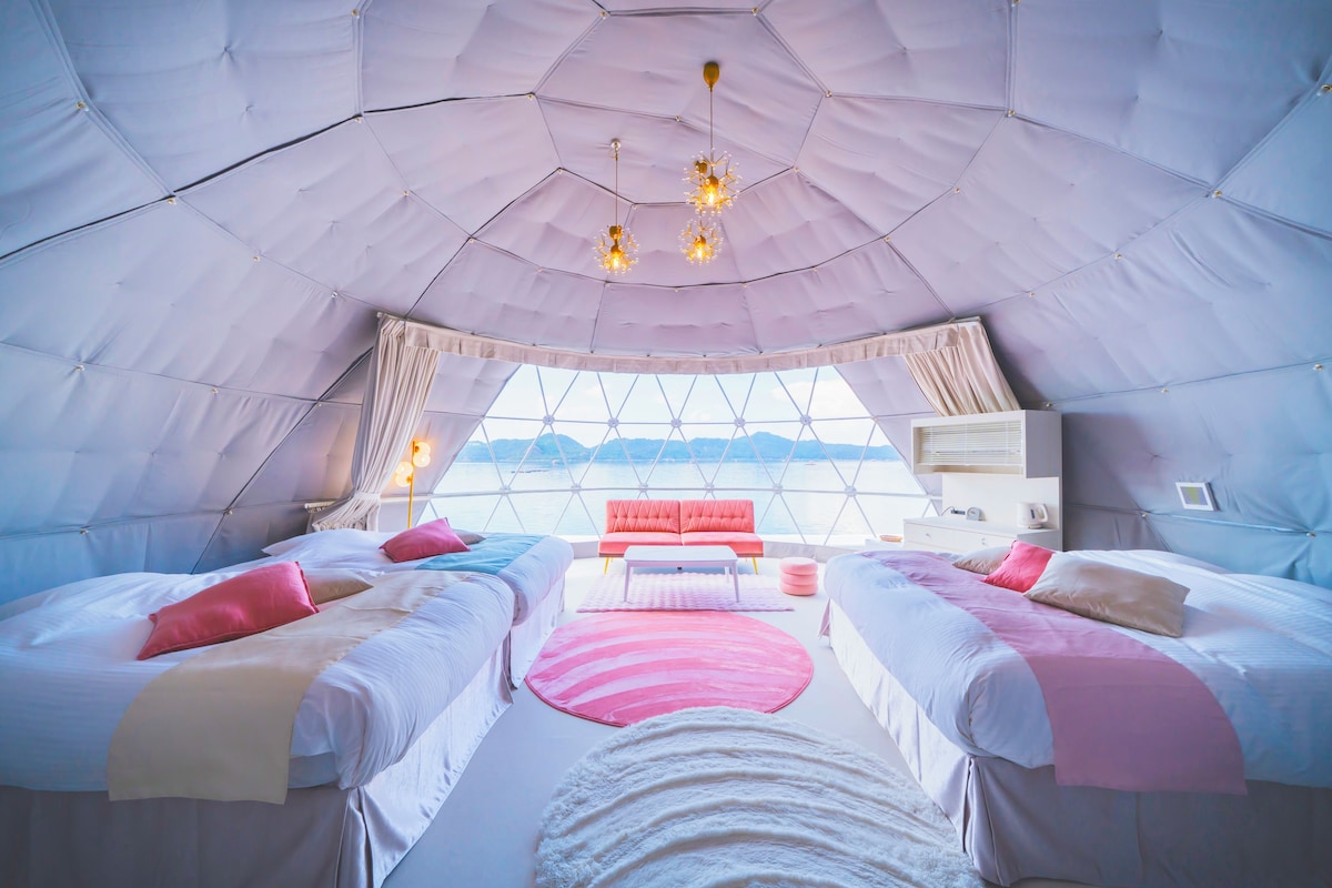 A tent-style room with two beds, a central table, and a view of the outdoors.