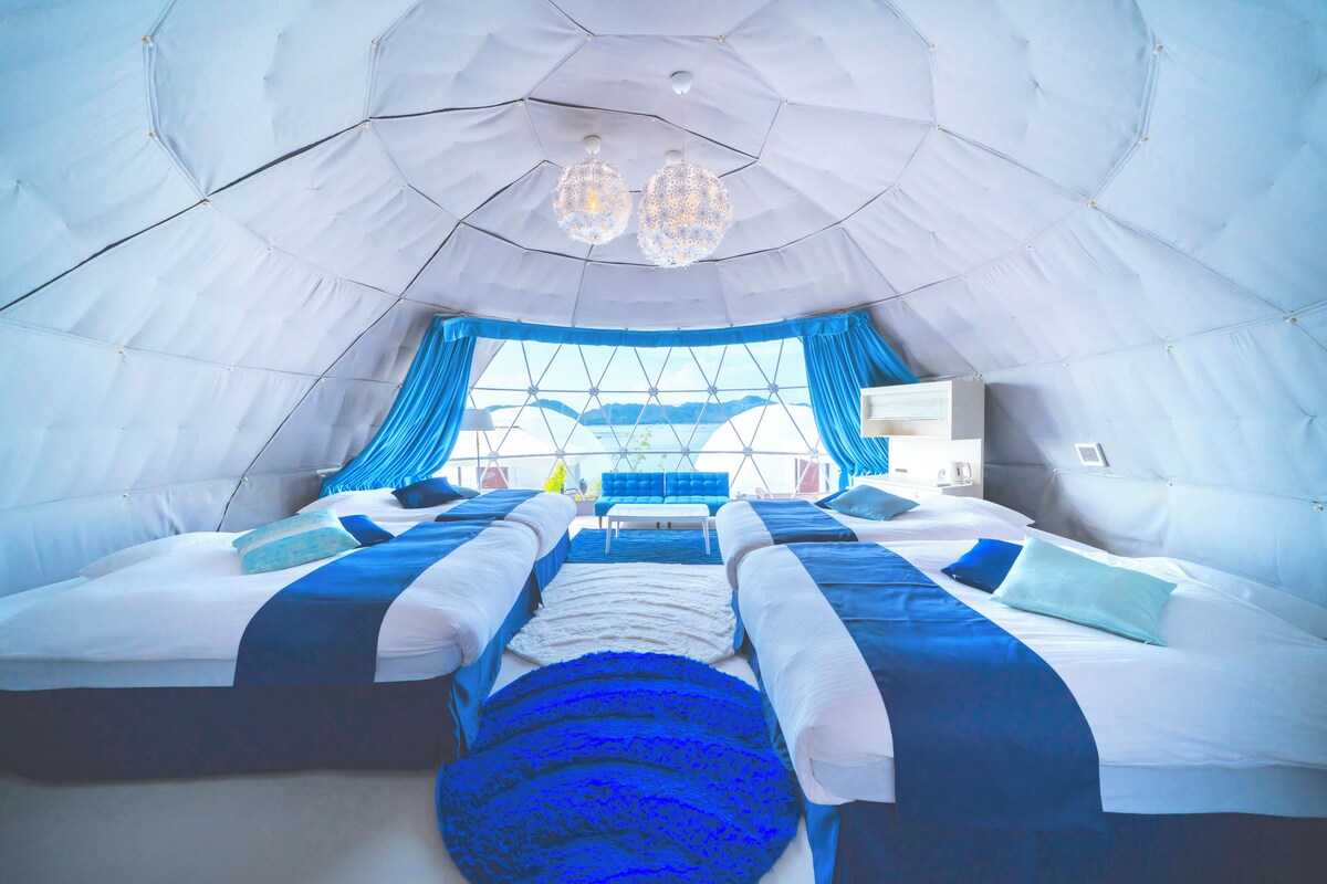 A tent-style room with two beds, a large window, and a chandelier.