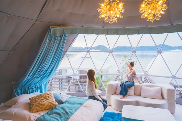 A room with a bed, a sofa, and a view of a body of water through a large window.