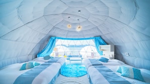 A tent-like interior with two beds, a central rug, and a view of the outdoors.
