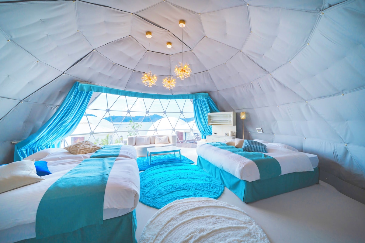A tent-style accommodation with two beds, a sofa, a coffee table, and a view through a large window.