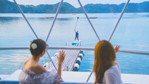 A boat with a person paddleboarding in the distance, two people observing from the boat, and a calm water body with hills in the background. - GLAMPREMIER Naruto (Naruto-shi Naruto-cho)