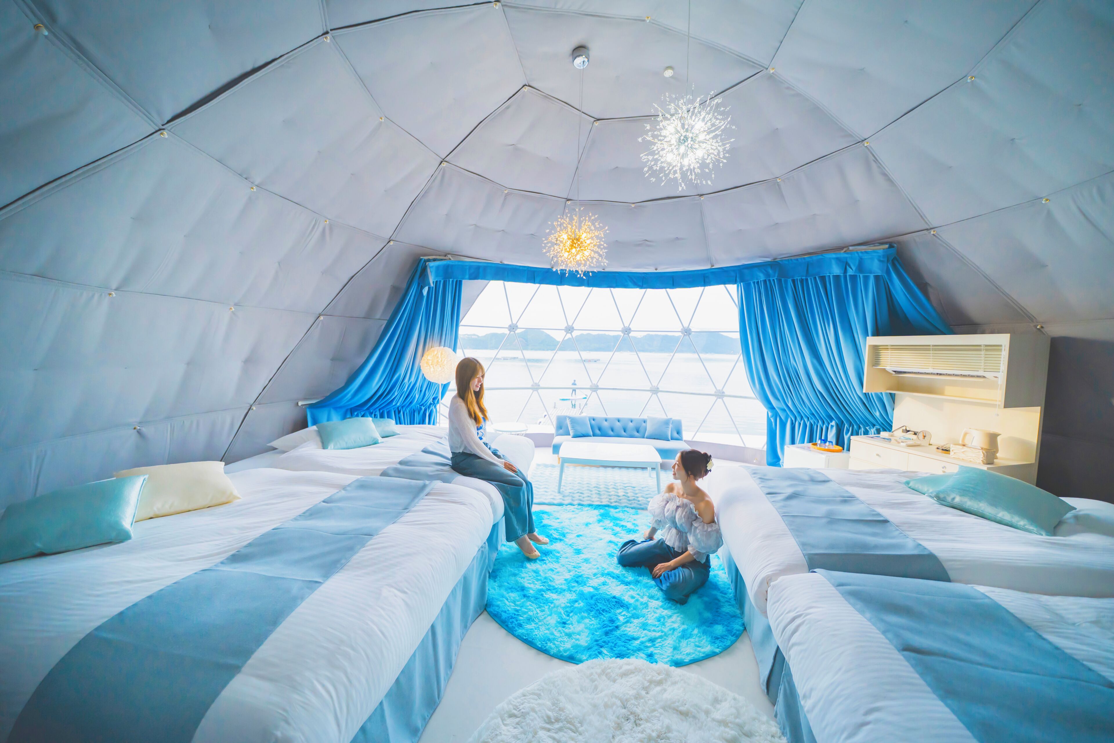 Une pièce aménagée comme une tente, avec deux lits, un espace salon central et une vue sur l’extérieur grâce à une grande fenêtre.